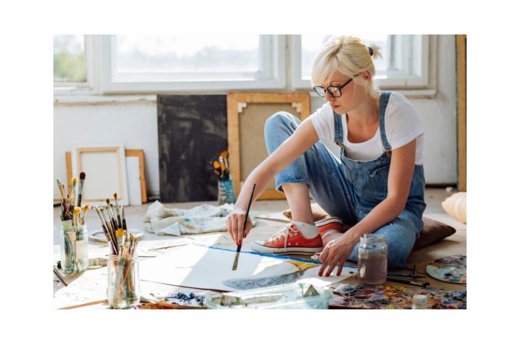 Woman sitting on the floor painting on a canvas