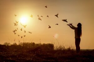 Woman releasing birds in a field at sunrise.