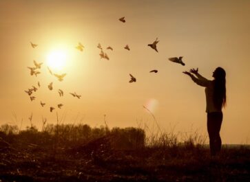 Woman releasing birds in a field at sunrise.